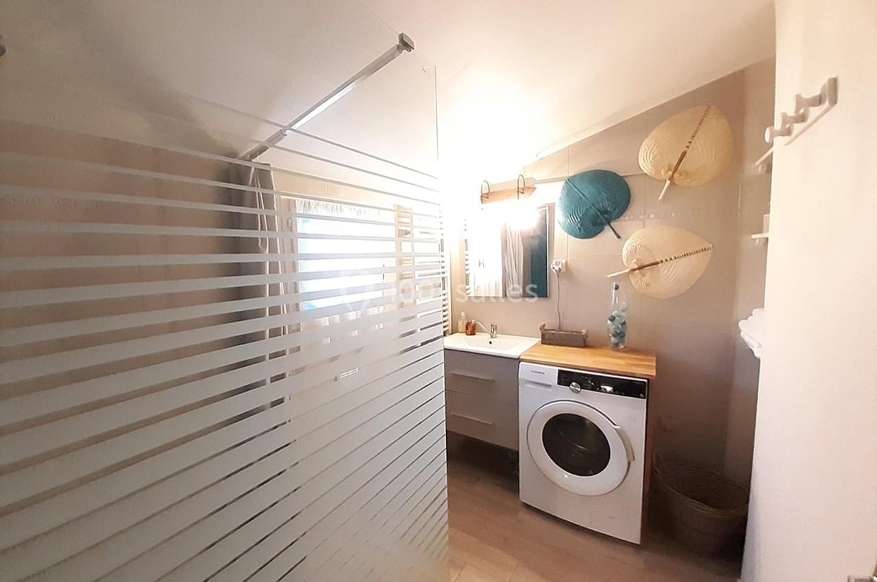 Salle de bain avec douche vitrée, meuble lavabo, machine à laver et décoration murale en ombrelles.