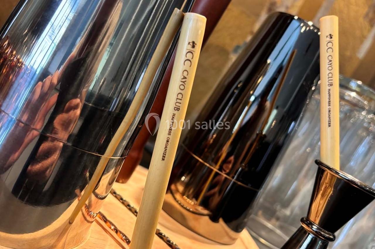 Deux shakers métalliques brillants et des bâtons en bois gravés ’ICC Cayo Club’ posés sur une surface en bois.