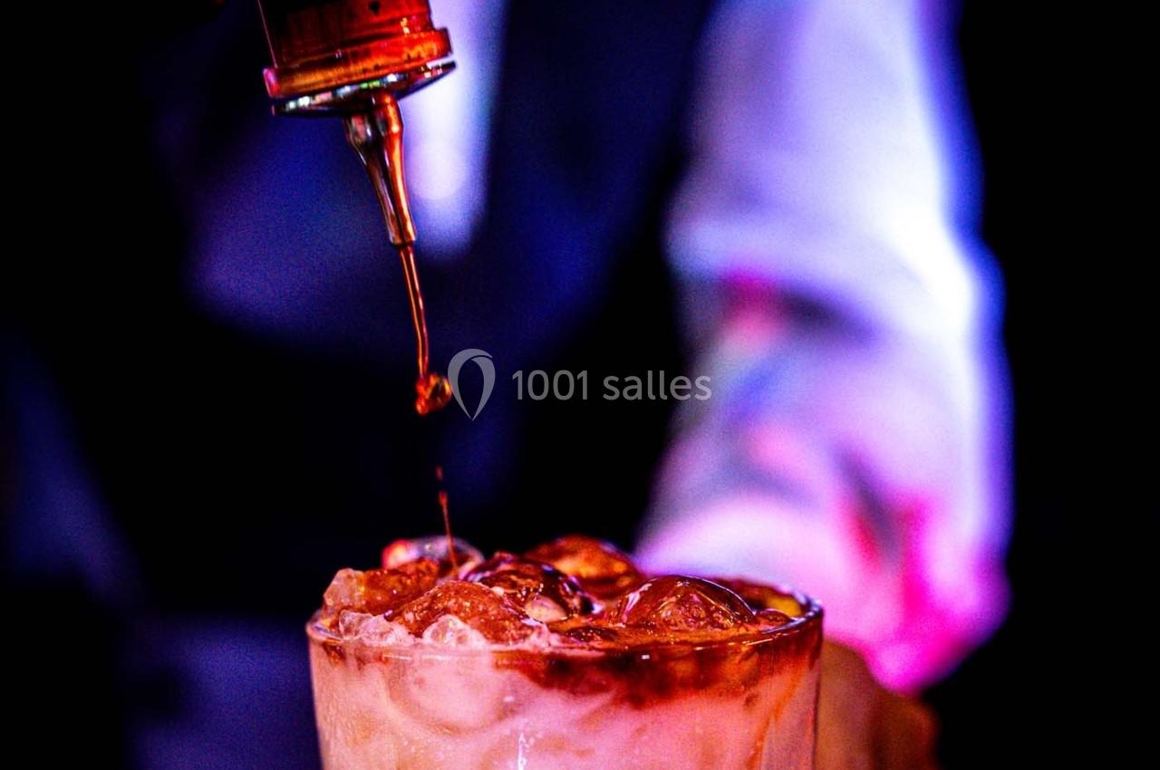 Un liquide ambré est versé sur des glaçons dans un verre, avec un arrière-plan flou et coloré.