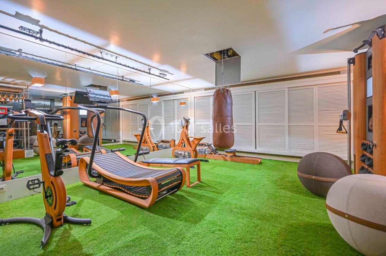 Salle de sport équipée avec machines en bois, sac de frappe, ballon de fitness et sol en gazon synthétique.