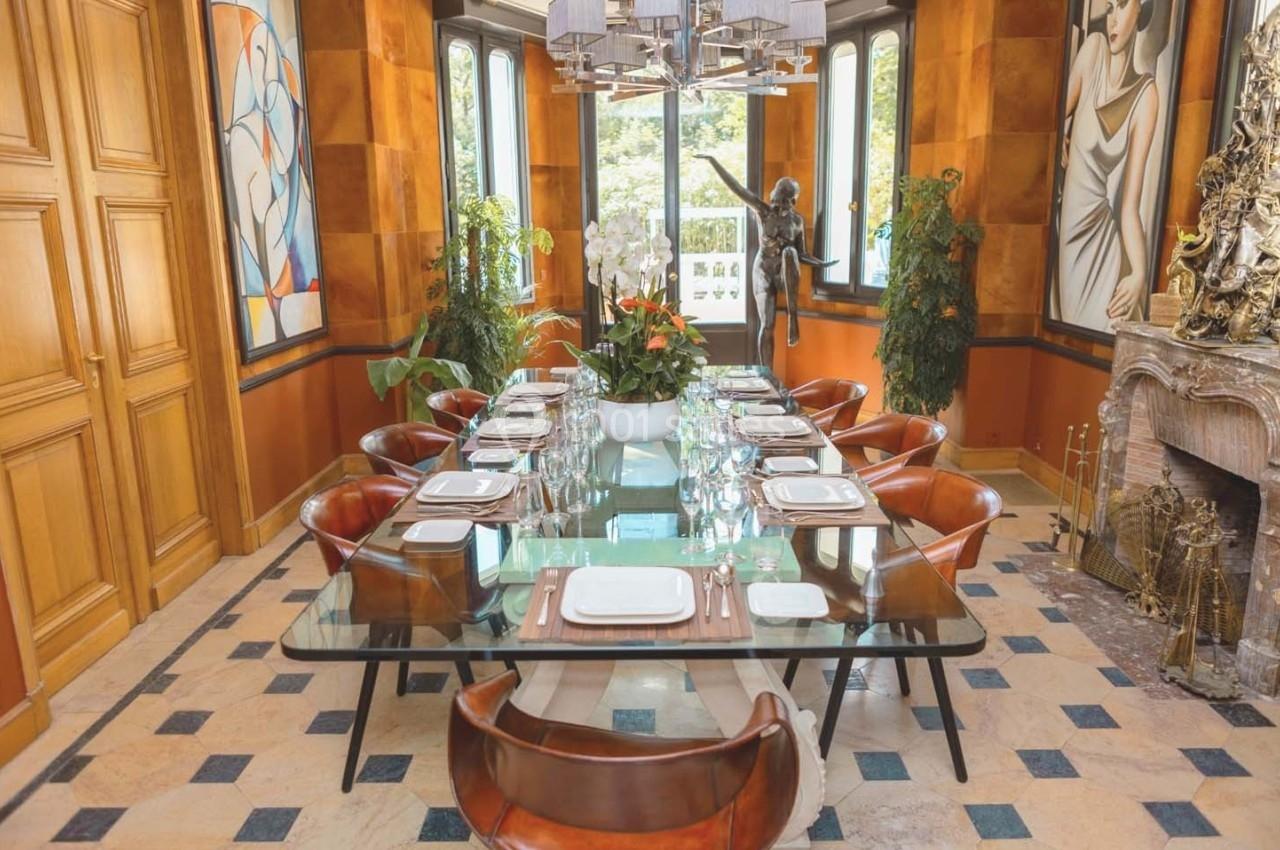 Salle à manger élégante avec une grande table en verre, des chaises en cuir, une cheminée et des œuvres d'art aux murs.