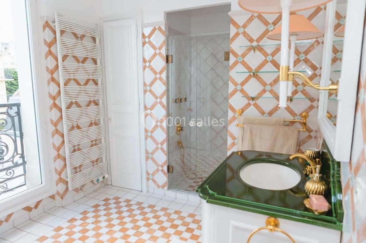 Salle de bain lumineuse avec carrelage à motifs orange et blanc, douche vitrée, lavabo vert et accessoires dorés.