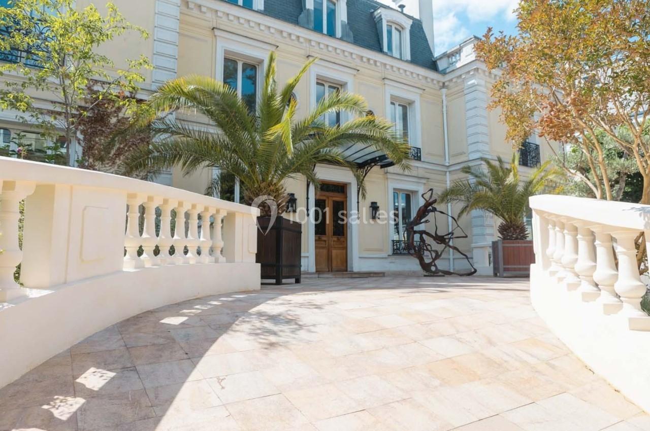 Façade d'un bâtiment élégant avec des palmiers, une sculpture moderne et une entrée bordée de balustrades.