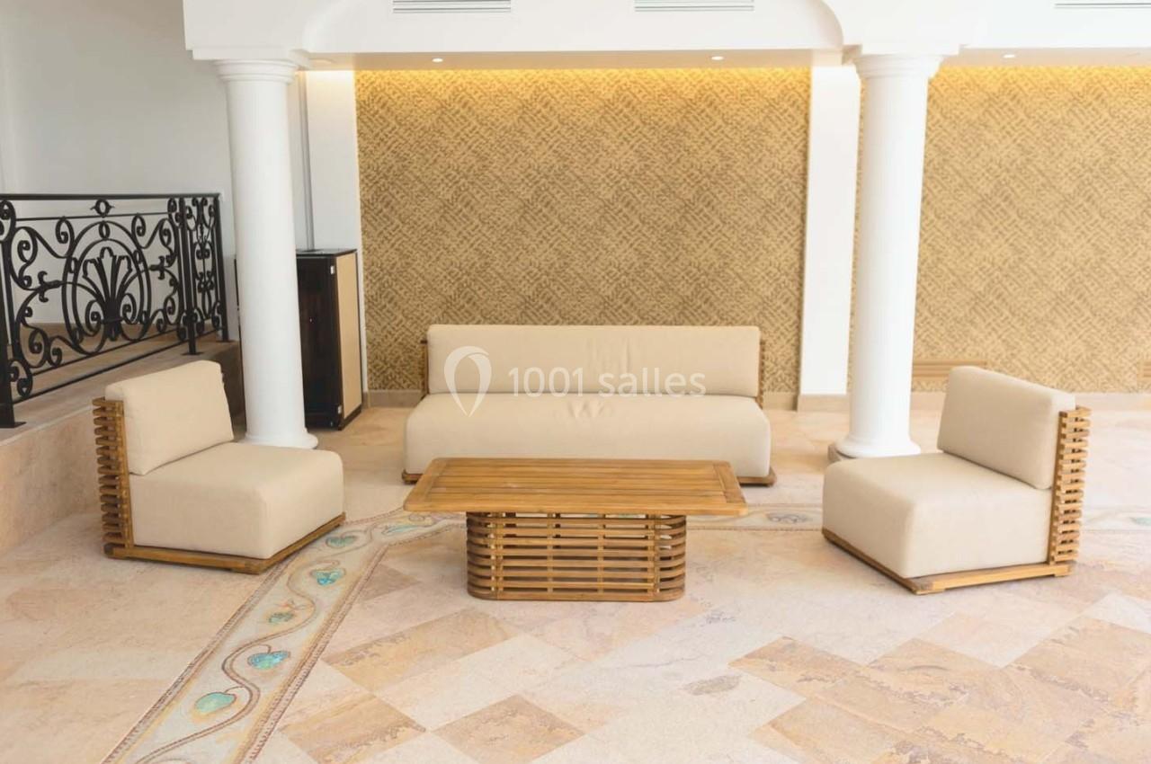 Mobilier de salon avec canapé, fauteuils et table basse en bois, disposés sur un sol en pierre dans un espace lumineux.