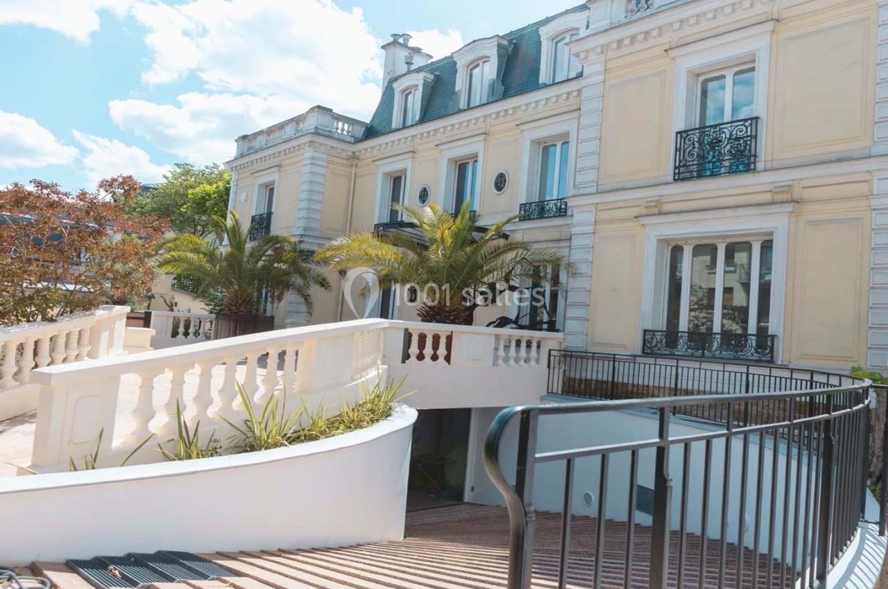 Façade d'un bâtiment élégant de style classique avec balustrades blanches, palmiers et ciel dégagé en arrière-plan.