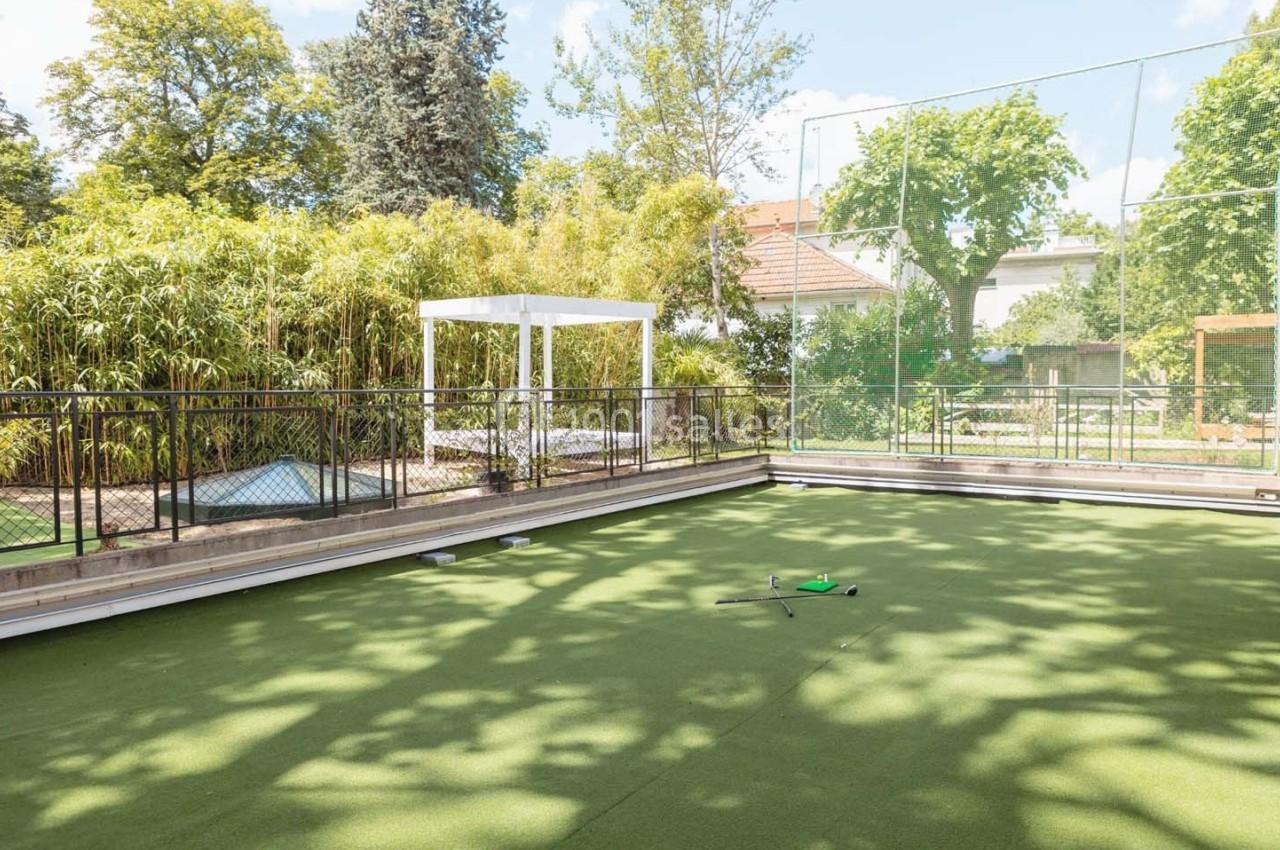 Terrain de sport extérieur en gazon synthétique, entouré de végétation et clôturé, avec un équipement au sol.