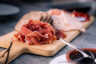 Plateau en bois avec des tranches de jambon cru, pain et autres charcuteries, posé sur une table grise.