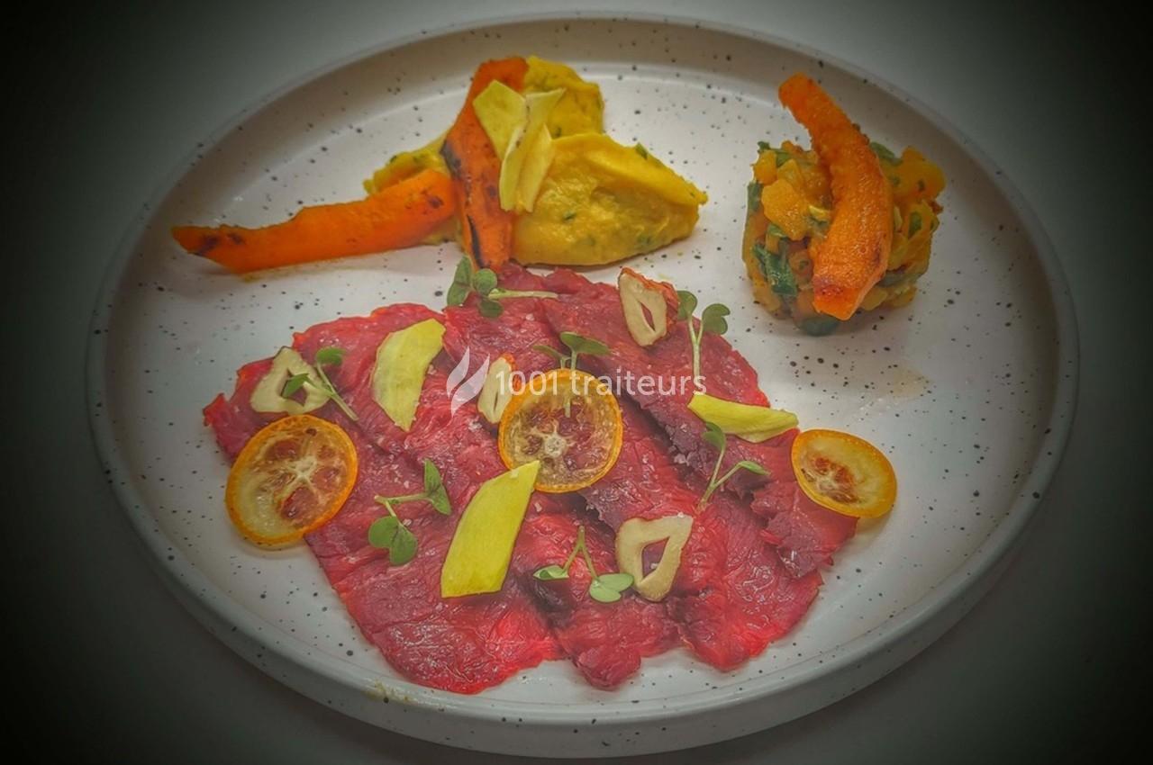 Assiette de carpaccio de bœuf avec rondelles de citron, légumes rôtis et purée colorée.
