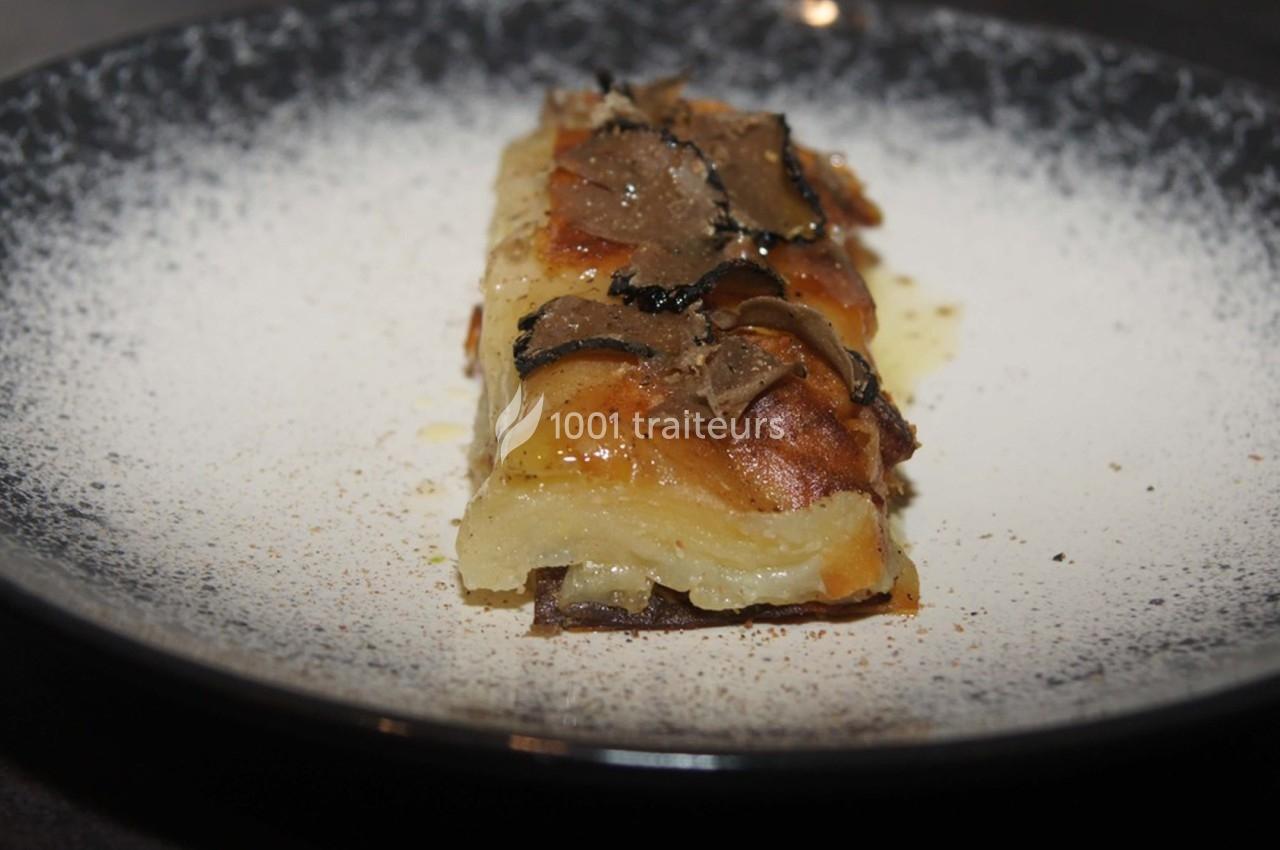 Part de gratin de pommes de terre garnie de fines tranches de truffe, servie dans une assiette sombre.
