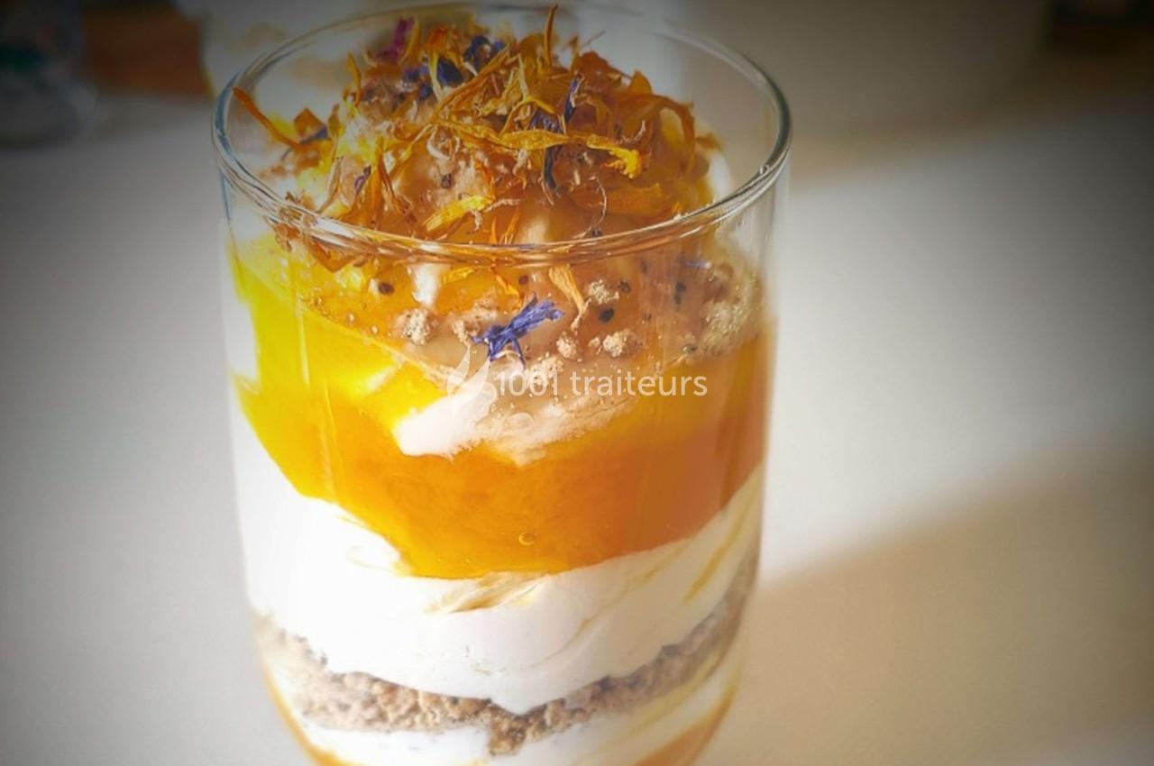 Verrine composée de couches de yaourt, purée de mangue, granola et fleurs comestibles en décoration.