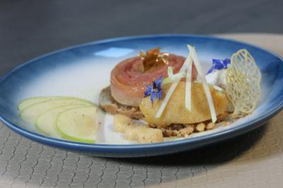 Dessert raffiné composé de pommes, crumble, fleurs comestibles et décorations, présenté sur une assiette bleue.