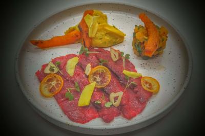 Assiette de carpaccio de bœuf avec rondelles de citron, légumes rôtis et purée colorée.