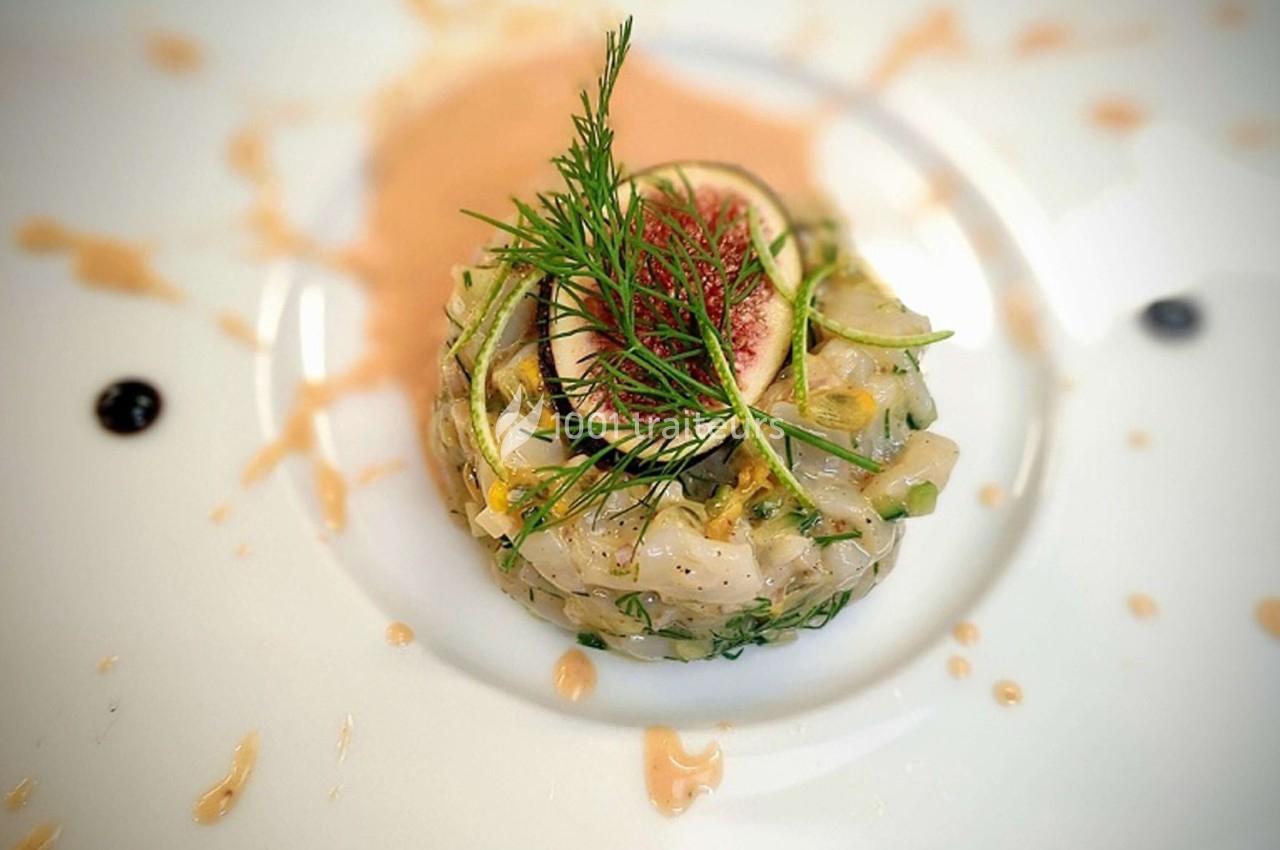 Tartare de poisson blanc garni de figue, courgette râpée et aneth, présenté sur une assiette avec une sauce décorative.