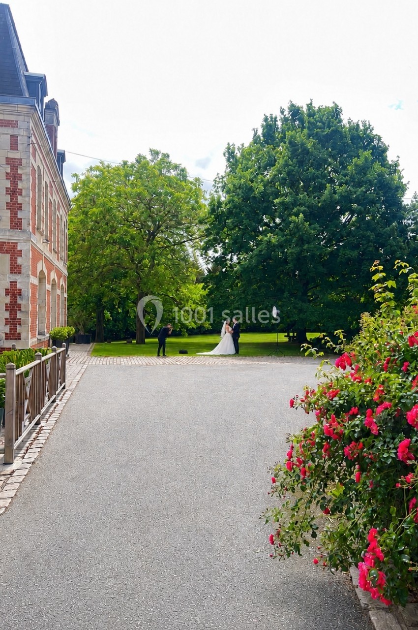 Un couple en tenue de mariage pose pour une photo dans un jardin près d'un bâtiment en briques.