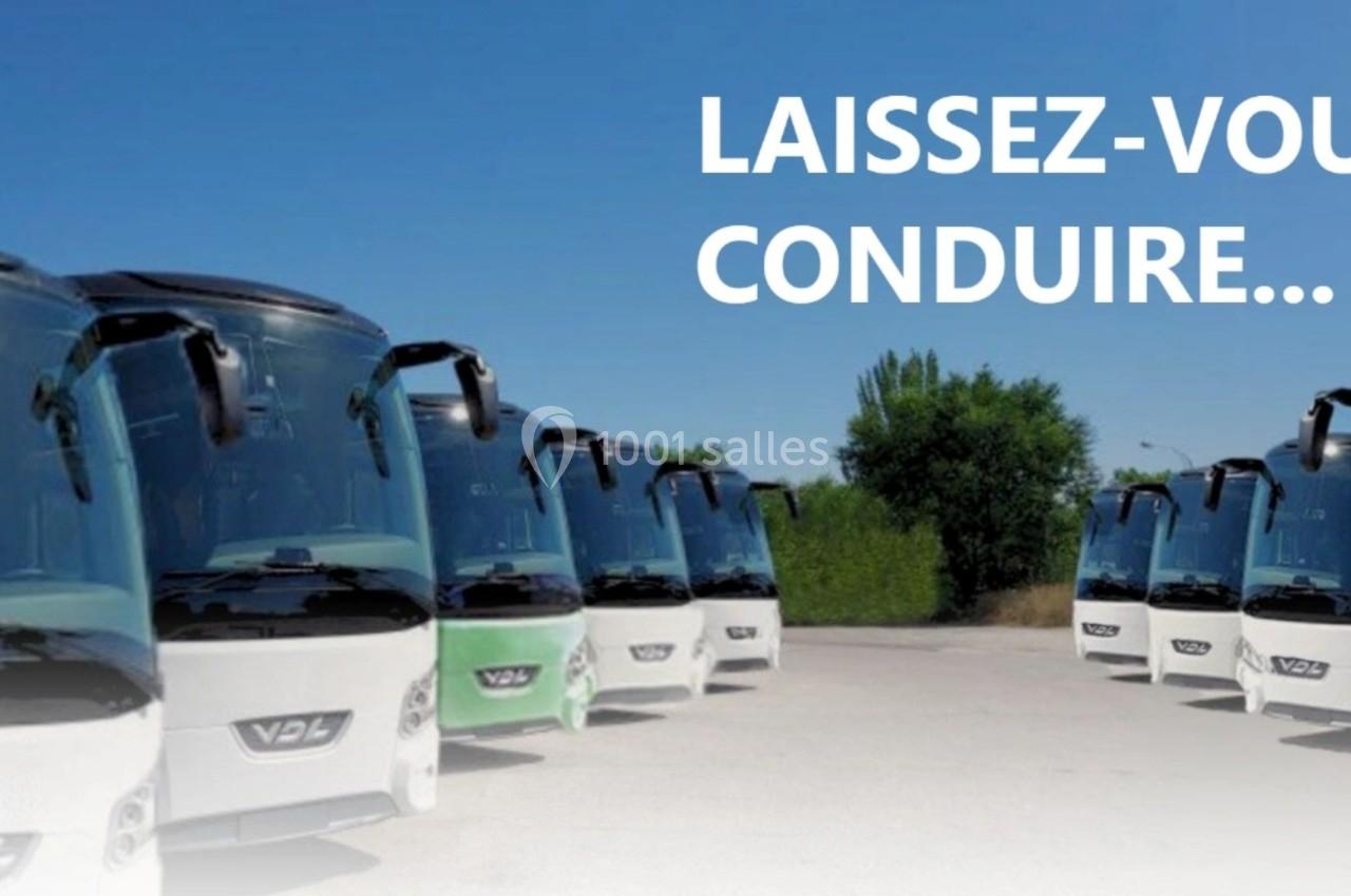 Alignement de plusieurs bus blancs stationnés sur un parking, avec un ciel bleu en arrière-plan.