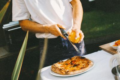 Un homme retire une pizza du four à l'aide d'une pelle, accompagné d'une femme souriante dans une cuisine moderne.