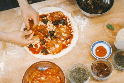 Un homme retire une pizza du four à l'aide d'une pelle, accompagné d'une femme souriante dans une cuisine moderne.