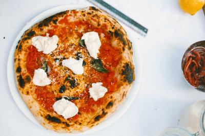 Un homme retire une pizza du four à l'aide d'une pelle, accompagné d'une femme souriante dans une cuisine moderne.