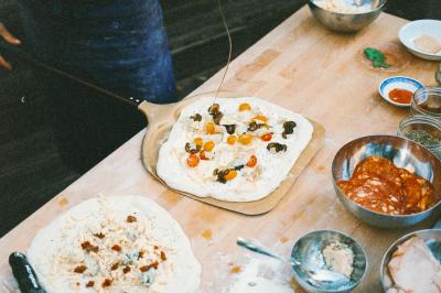 Un homme retire une pizza du four à l'aide d'une pelle, accompagné d'une femme souriante dans une cuisine moderne.