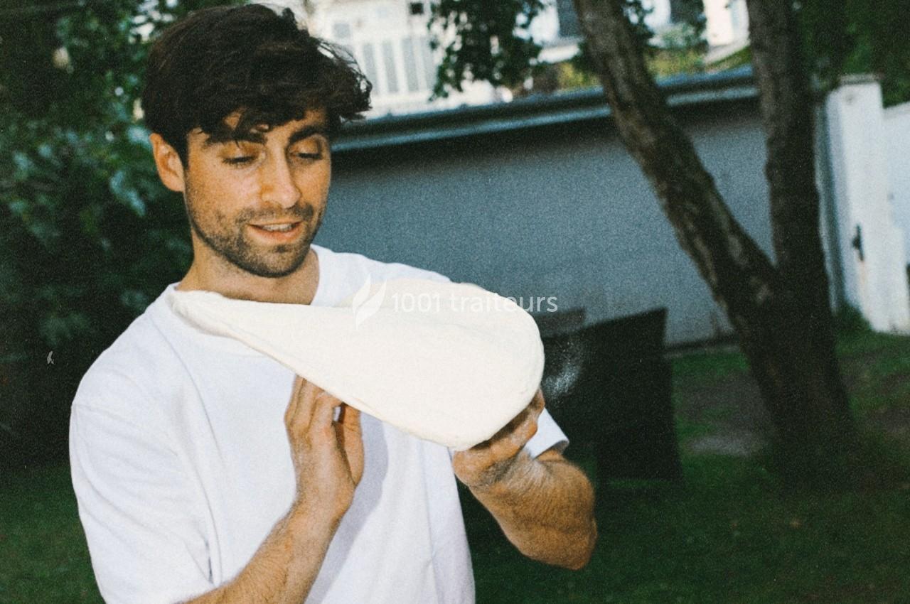 Un homme en t-shirt blanc manipule une pâte à pizza dans un jardin.