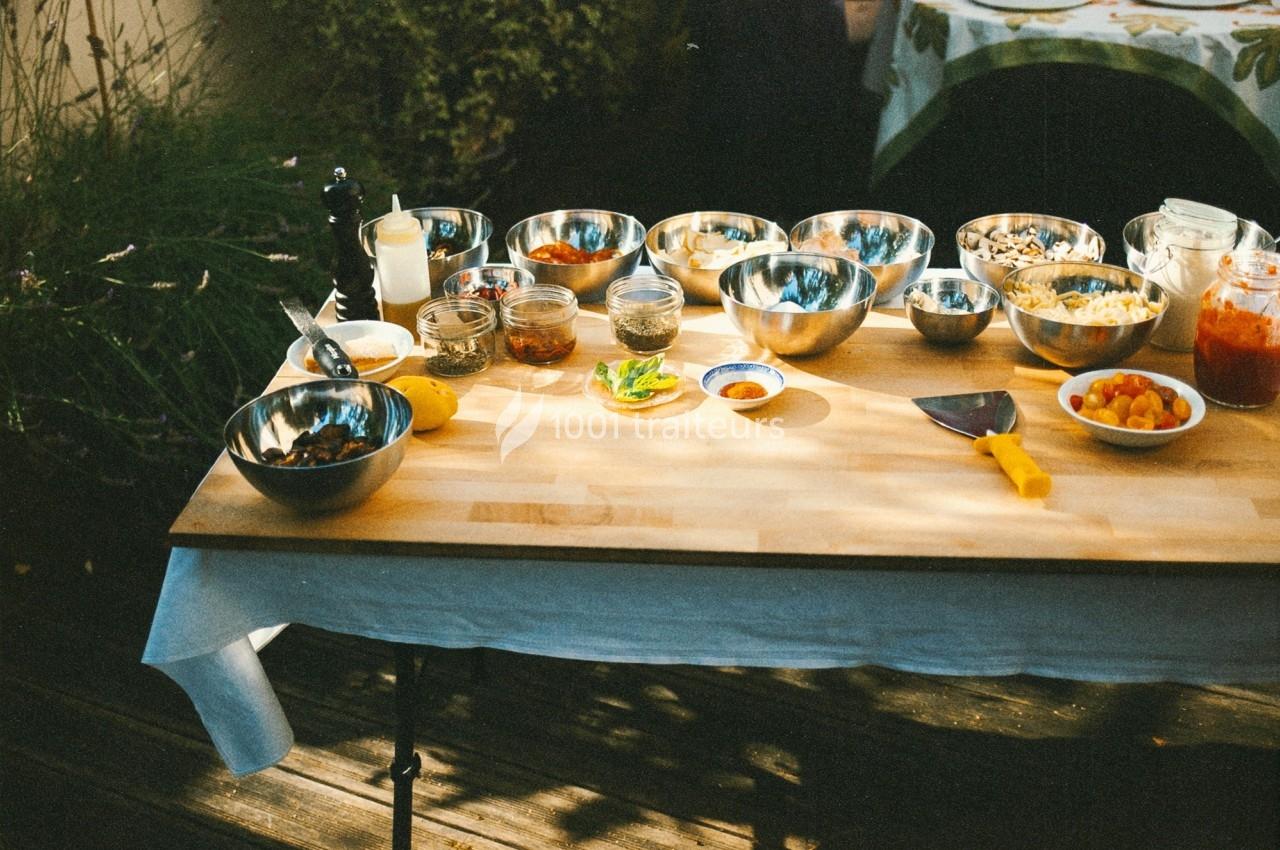 Table en bois avec divers bols, pots et ingrédients disposés pour la préparation culinaire en extérieur.
