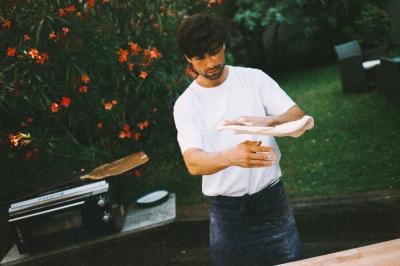 Un homme retire une pizza du four à l'aide d'une pelle, accompagné d'une femme souriante dans une cuisine moderne.