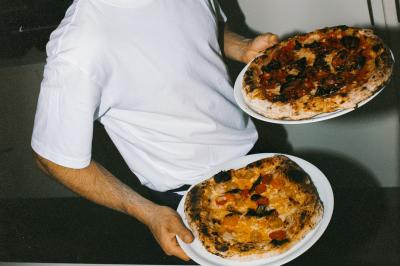 Un homme retire une pizza du four à l'aide d'une pelle, accompagné d'une femme souriante dans une cuisine moderne.
