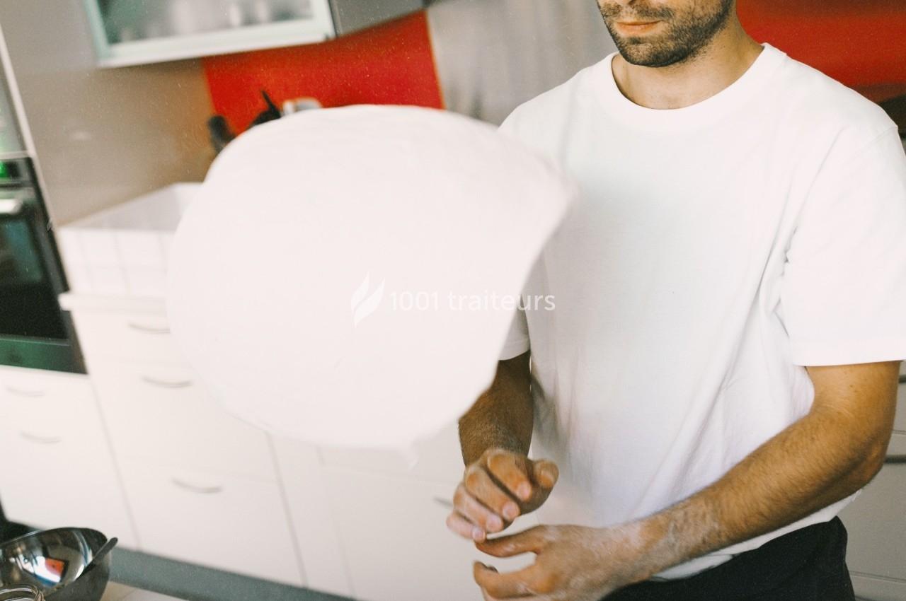 Un homme fait tourner une pâte à pizza dans une cuisine moderne avec un mur rouge en arrière-plan.