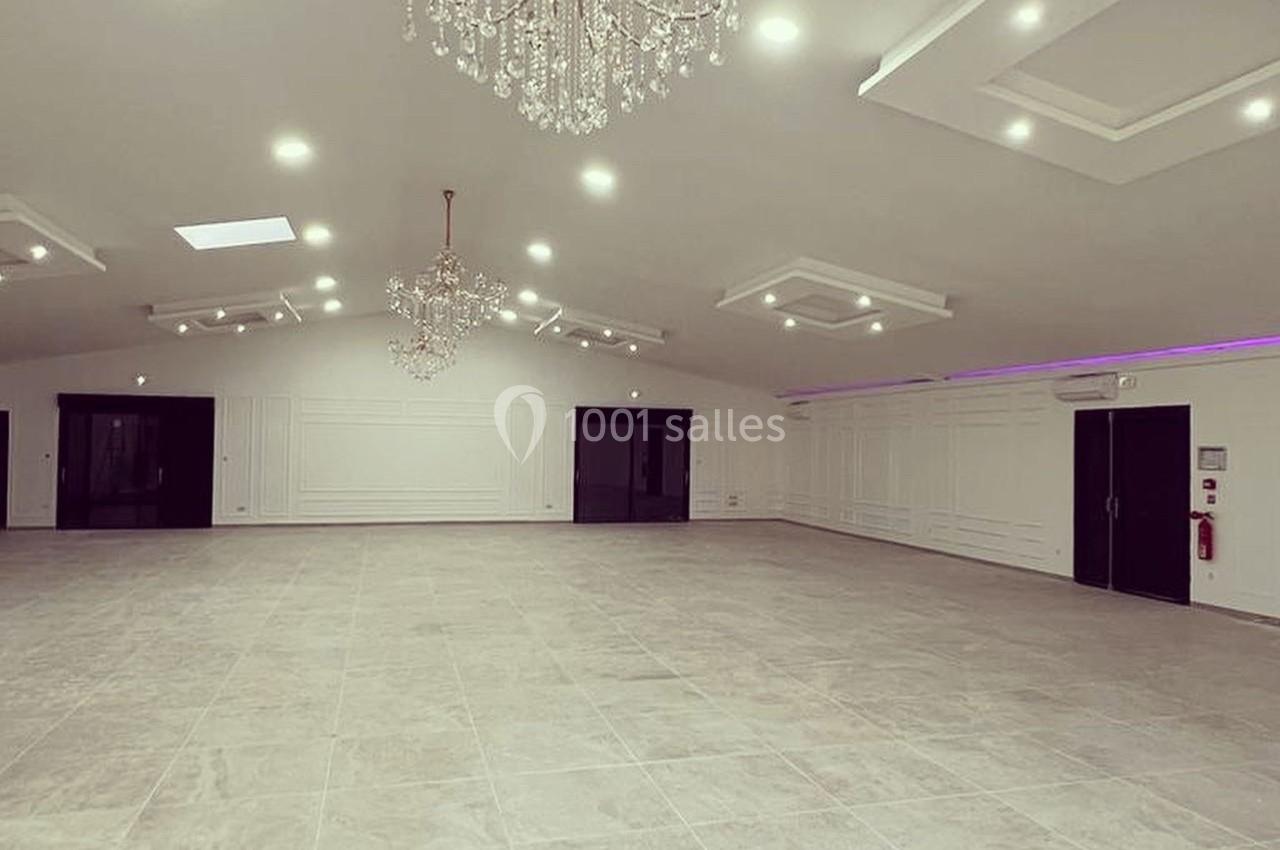 Salle spacieuse avec sol en carrelage clair, murs blancs, plafonds avec moulures et lustres en cristal suspendus.