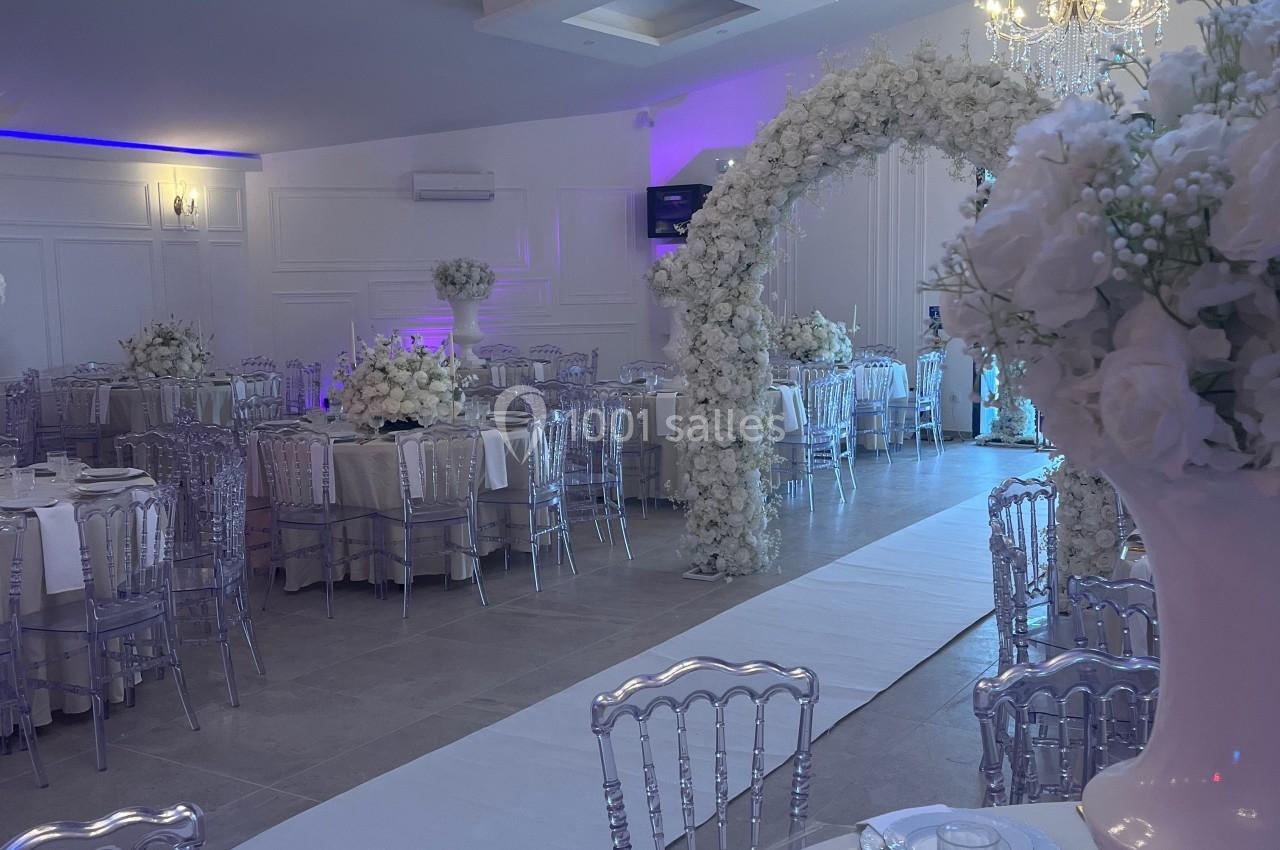Salle de réception décorée avec des tables élégantes, des chaises transparentes, des fleurs blanches et un éclairage tamisé.