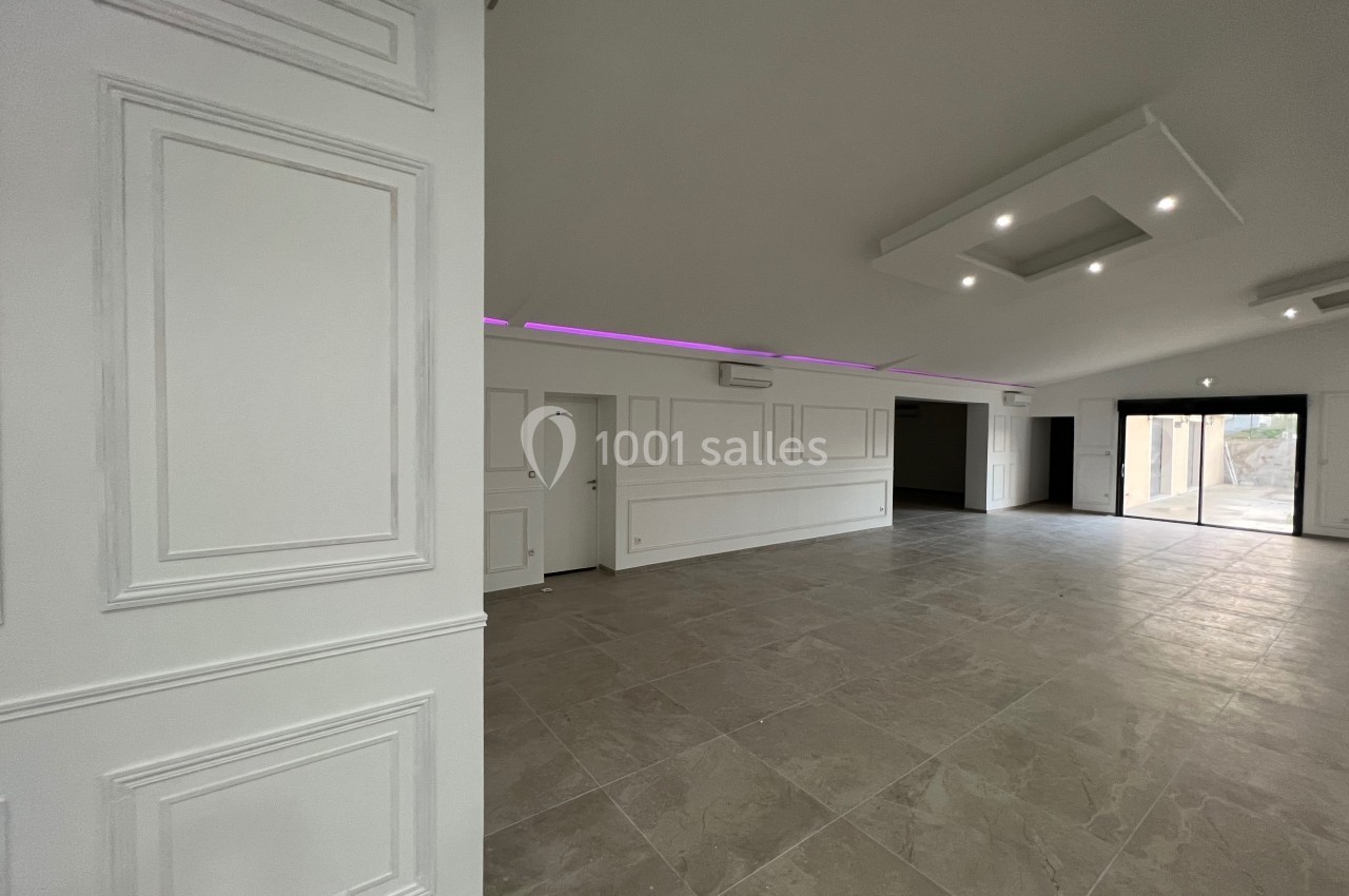 Salle spacieuse avec sol en carrelage, murs blancs ornés de moulures et éclairage encastré au plafond.