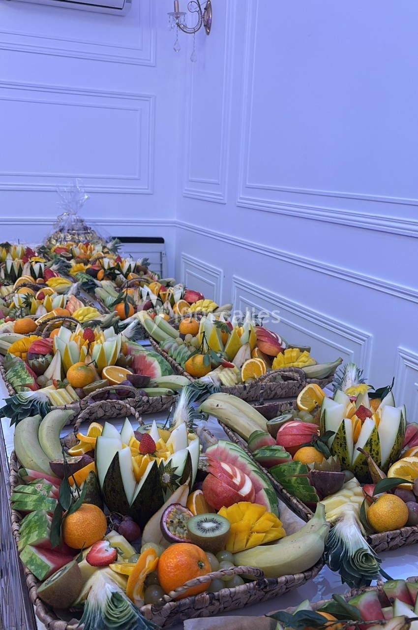 Plateau de fruits variés joliment découpés et disposés sur une longue table dans une salle blanche élégante.
