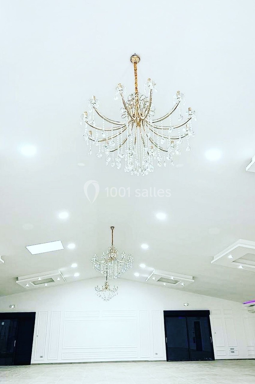 Salle spacieuse avec plafond blanc, lustres en cristal suspendus et murs ornés de moulures.