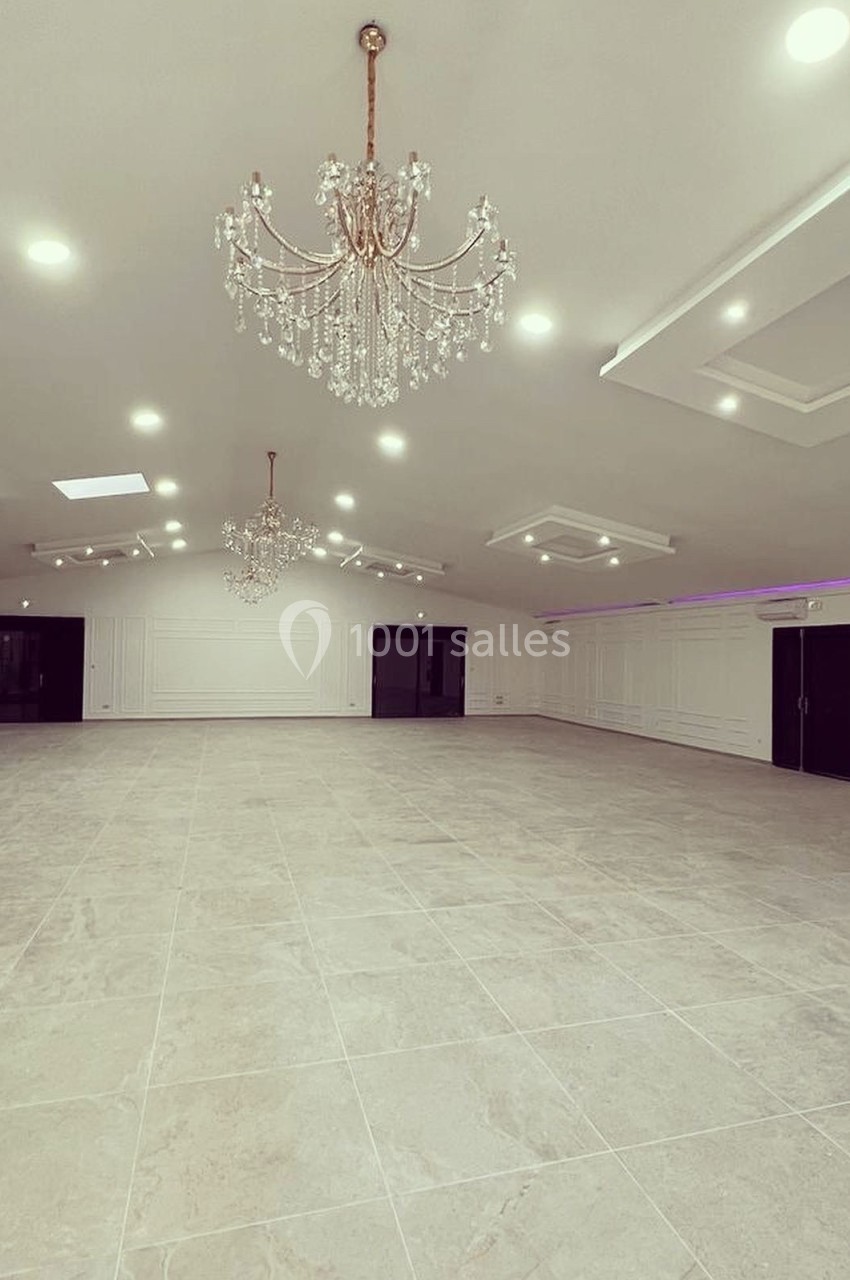 Salle spacieuse avec sol en carrelage clair, murs blancs, lustres suspendus et éclairage encastré au plafond.