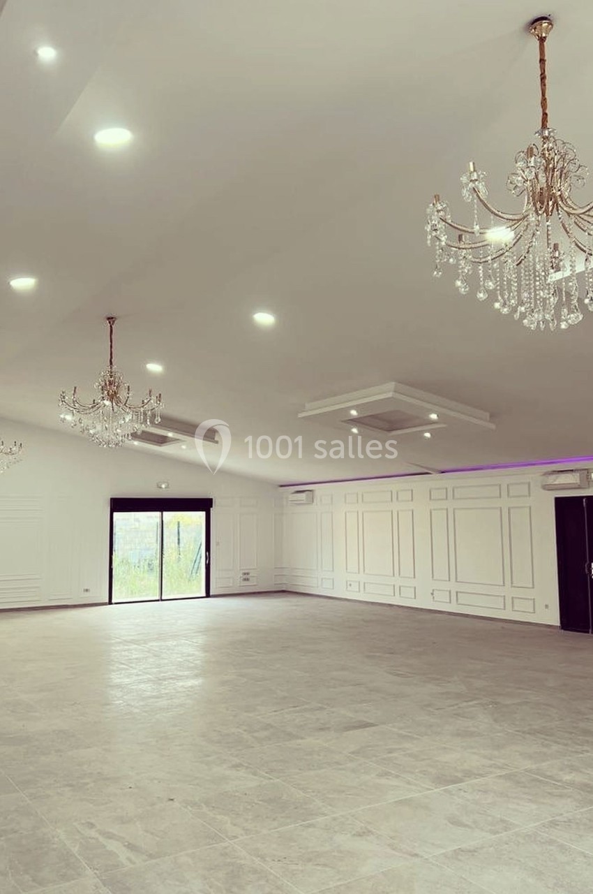 Salle spacieuse avec sol en carrelage, murs blancs, lustres en cristal et éclairage moderne au plafond.
