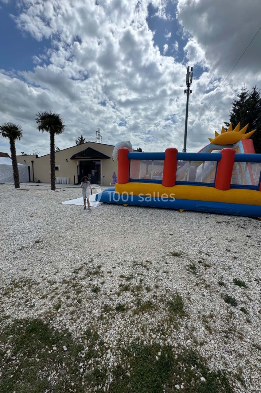Structure gonflable colorée sur un sol gravillonné, avec un enfant à proximité et un bâtiment en arrière-plan.