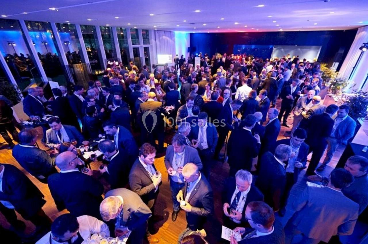 Groupe de personnes en tenue professionnelle réunies lors d'un événement dans une grande salle éclairée.