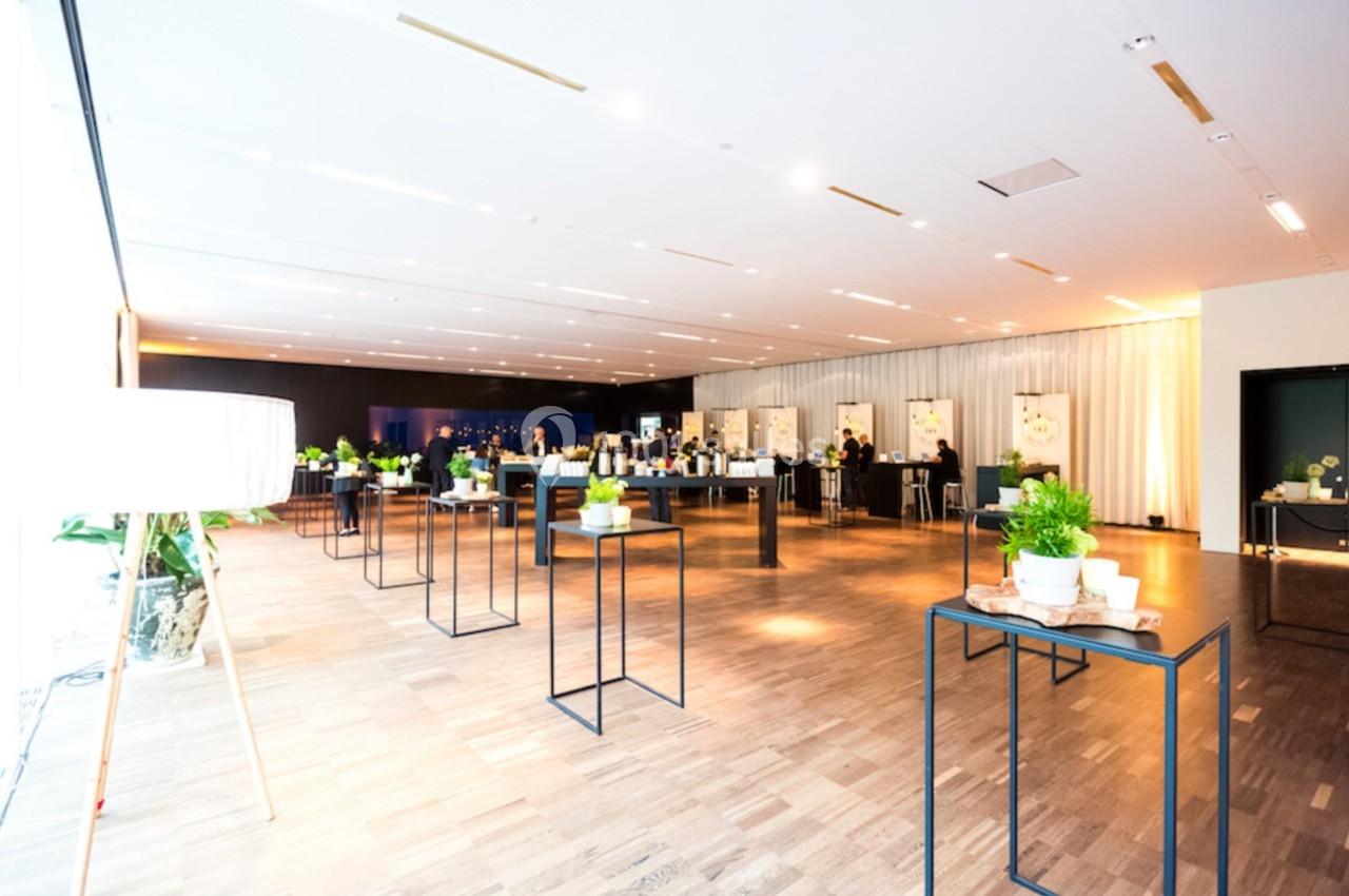 Salle lumineuse avec tables hautes décorées de plantes, espace aménagé pour un événement ou une réception.