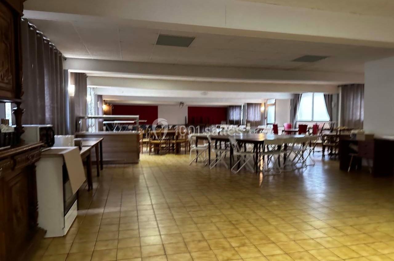 Salle spacieuse avec tables et chaises disposées pour un événement, sol en carrelage jaune et lumière naturelle.