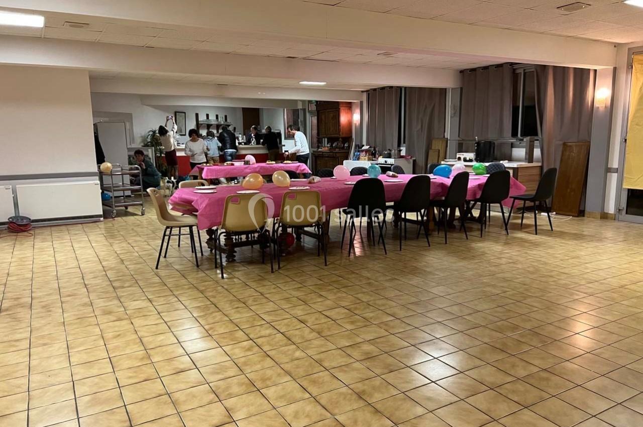 Salle avec tables recouvertes de nappes roses, chaises disposées autour et quelques personnes en arrière-plan.