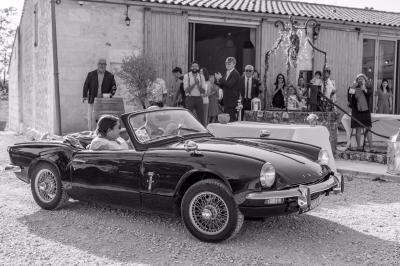 Façade d'une maison en pierre avec terrasse ensoleillée, chaises longues et pots de fleurs sur un sol pavé clair.