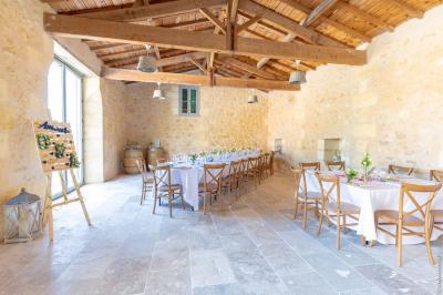 Façade d'une maison en pierre avec terrasse ensoleillée, chaises longues et pots de fleurs sur un sol pavé clair.