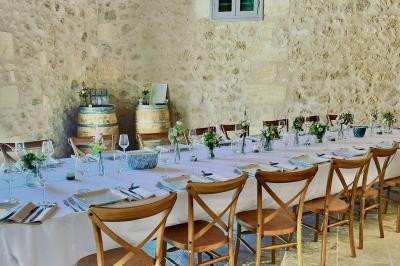 Façade d'une maison en pierre avec terrasse ensoleillée, chaises longues et pots de fleurs sur un sol pavé clair.