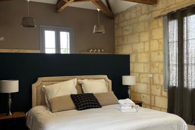 Façade d'une maison en pierre avec terrasse ensoleillée, chaises longues et pots de fleurs sur un sol pavé clair.