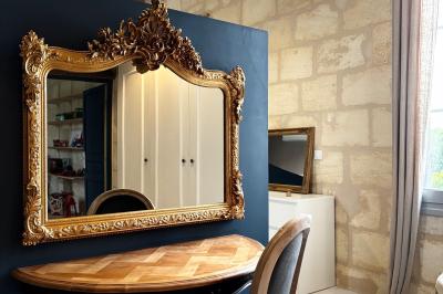 Façade d'une maison en pierre avec terrasse ensoleillée, chaises longues et pots de fleurs sur un sol pavé clair.