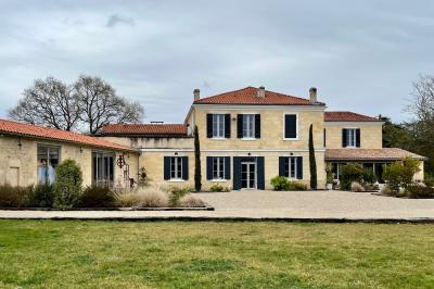 Façade d'une maison en pierre avec terrasse ensoleillée, chaises longues et pots de fleurs sur un sol pavé clair.