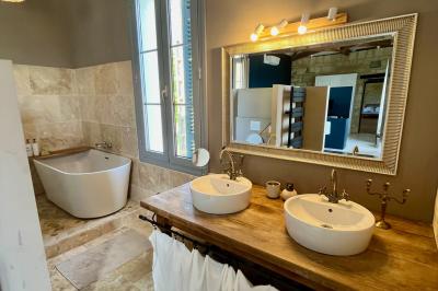 Façade d'une maison en pierre avec terrasse ensoleillée, chaises longues et pots de fleurs sur un sol pavé clair.
