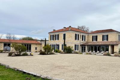 Façade d'une maison en pierre avec terrasse ensoleillée, chaises longues et pots de fleurs sur un sol pavé clair.