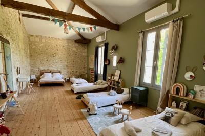 Façade d'une maison en pierre avec terrasse ensoleillée, chaises longues et pots de fleurs sur un sol pavé clair.