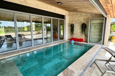 Façade d'une maison en pierre avec terrasse ensoleillée, chaises longues et pots de fleurs sur un sol pavé clair.